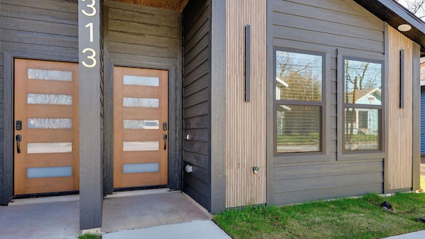 A modern two-story building with a gray exterior, two wooden doors with glass panels, and large windows.