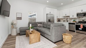 A modern living room with a grey sectional sofa, a wooden coffee table, and a TV mounted on the wall.