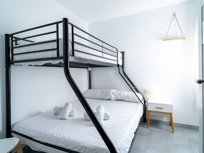 Ein Etagenbett mit weißer Bettwäsche und Handtüchern, ein Nachttisch mit Lampe und eine Pendelleuchte.