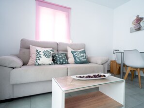 Ein modernes Wohnzimmer mit einer Couch, einem Glastisch und einem Essbereich mit Stühlen.