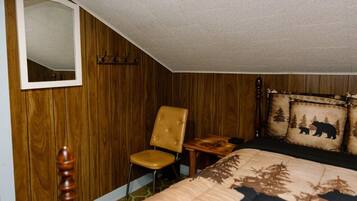 Un dormitorio con pared revestida de madera, un espejo, un sillón capitonado, una mesita de noche, una cama con un cojín con motivos de oso y una lámpara de pie de madera.