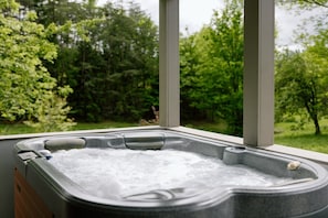 Ein Whirlpool mit Blick auf eine grüne Landschaft durch große Fenster.