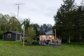 Ein zweigeschossiges Haus mit einer kleinen Veranda, einem Grill und einer Feuerstelle im Garten.