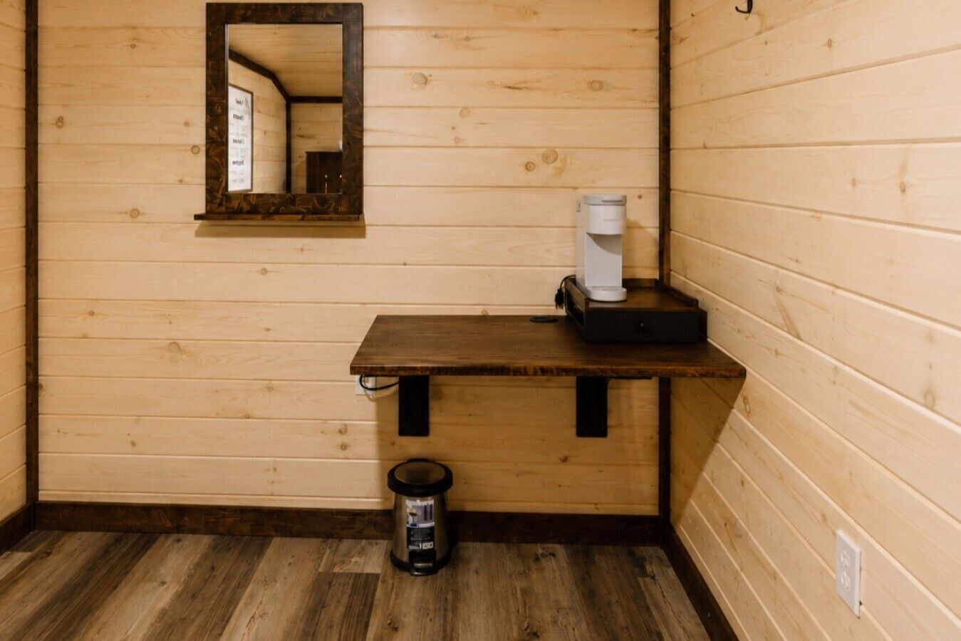 Une petite cabane en bois avec un seul banc en bois, une machine à café et une poubelle.