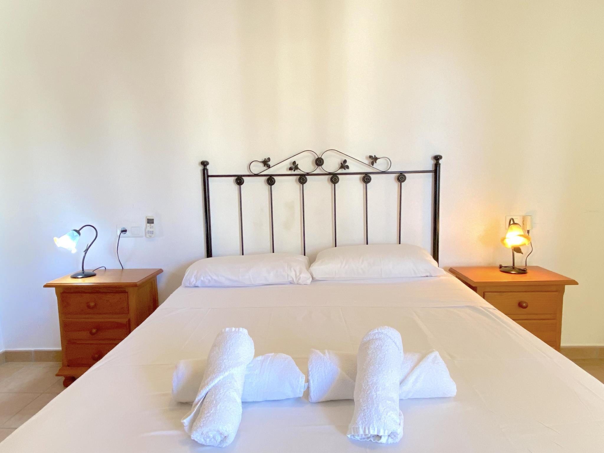 Un lit bien fait, avec du linge de lit et des serviettes blancs, deux tables de chevet avec des lampes et une simple tête de lit en métal.