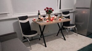 Un comedor con una mesa preparada para dos personas, un florero con flores, velas y una botella de vino.