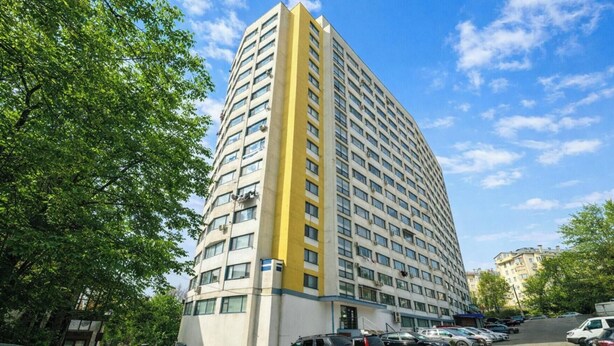 Un edificio alto de varios pisos con fachada curva, ventanas grandes y un detalle amarillo en la esquina.