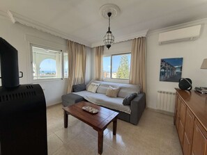 Un salon avec un canapé, une table basse et une vue sur la mer grâce à de grandes fenêtres.