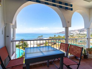 Ein Balkon mit Tisch und Stühlen, der Blick auf ein Schwimmbad und einen Strand freigibt.