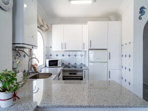 A modern kitchen with white cabinetry, a granite countertop, a built-in microwave, and a stainless steel sink. - Stella Maris Beachfront 3A by Casasol by Interhome (Nerja)