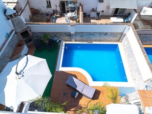 Ein Pool auf dem Dach mit glasklarer Wasserfläche, umgeben von einer Steinmauer und einer mit Fliesen ausgelegten Liegefläche mit Liegestühlen und Sonnenschirmen.