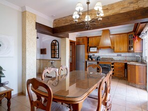 Eine geräumige Küche mit Holzschränken, einem Edelstahlkühlschrank und einem Essbereich mit einem Glastisch und Holzstühlen.