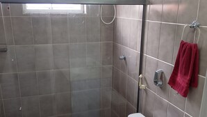 Un baño con ducha de vidrio, inodoro, lavamanos y una toalla roja colgada en un perchero.