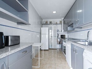 A modern kitchen with grey cabinets, a stainless steel microwave, a white refrigerator, and a granite countertop. - Apartment  by Interhome (Nerja)