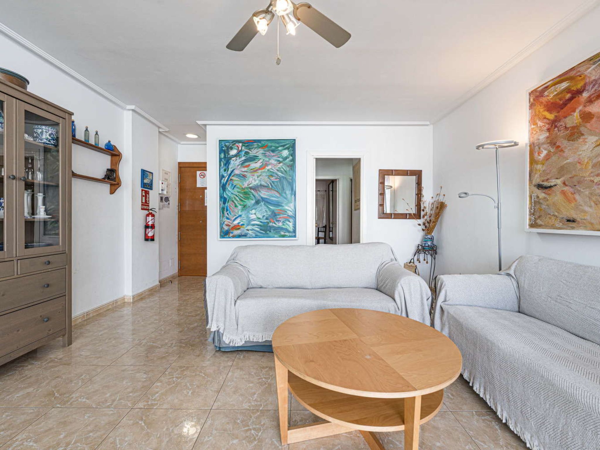 Uma sala de estar com sofá, mesa de centro, armário e ventilador de teto.