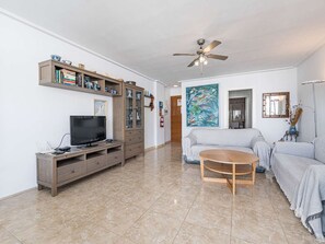 A living room with a TV, wooden entertainment unit, a ceiling fan, and a painting on the wall. - Apartment  by Interhome (Nerja)
