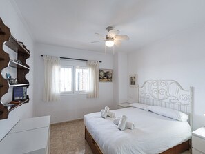 A bedroom with a bed, a ceiling fan, a window with curtains, a bedside table, and a wall-mounted shelf. - Apartment  by Interhome (Nerja)
