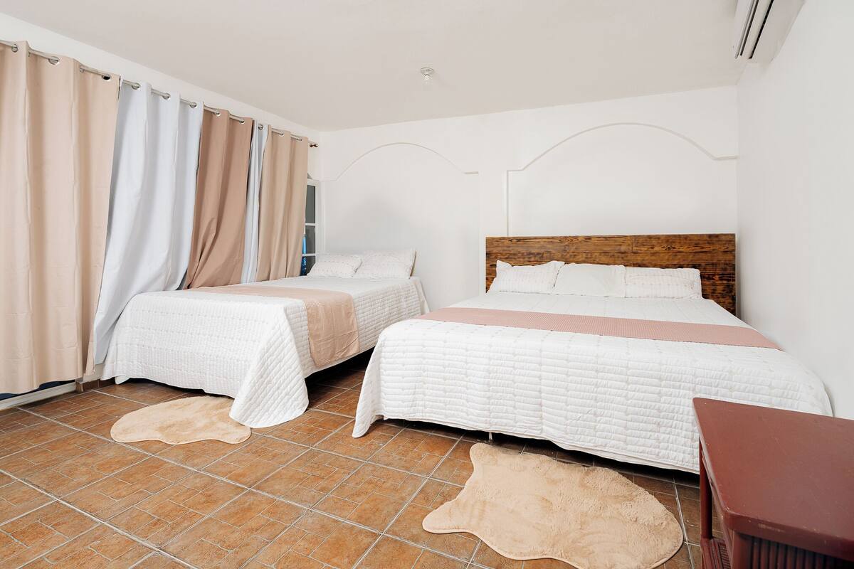 Un dormitorio con dos camas, cabeceros de madera, una ventana con cortinas y suelo de baldosas.