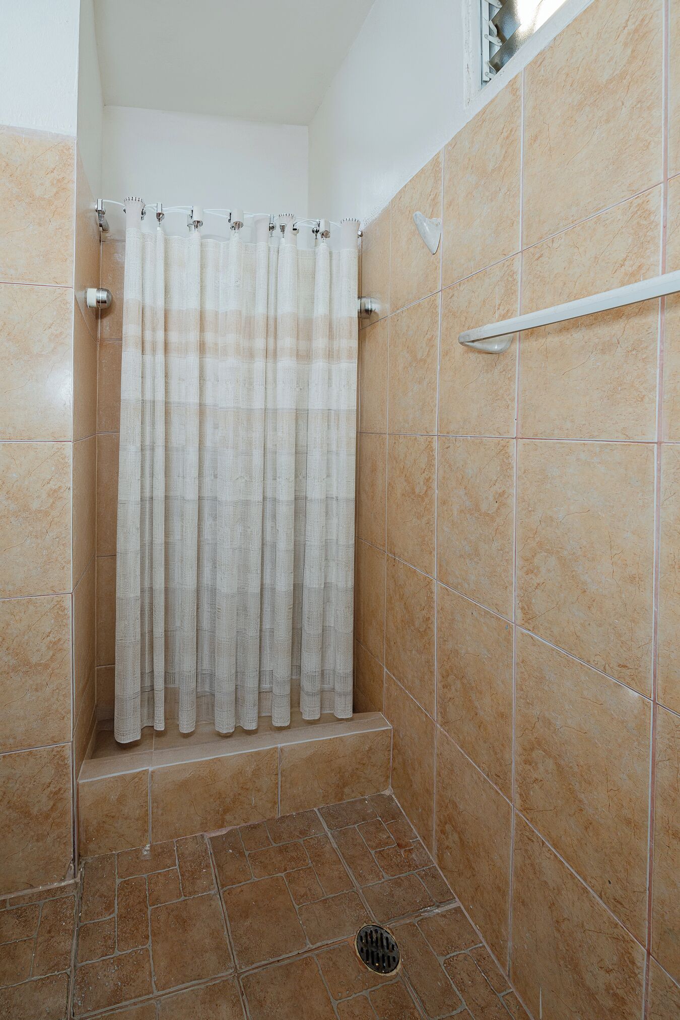 Un espace douche doté d’un rideau, de murs carrelés et d’une barre d’appui en métal.