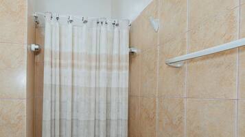 Un espace douche doté d’un rideau, de murs carrelés et d’une barre d’appui en métal.
