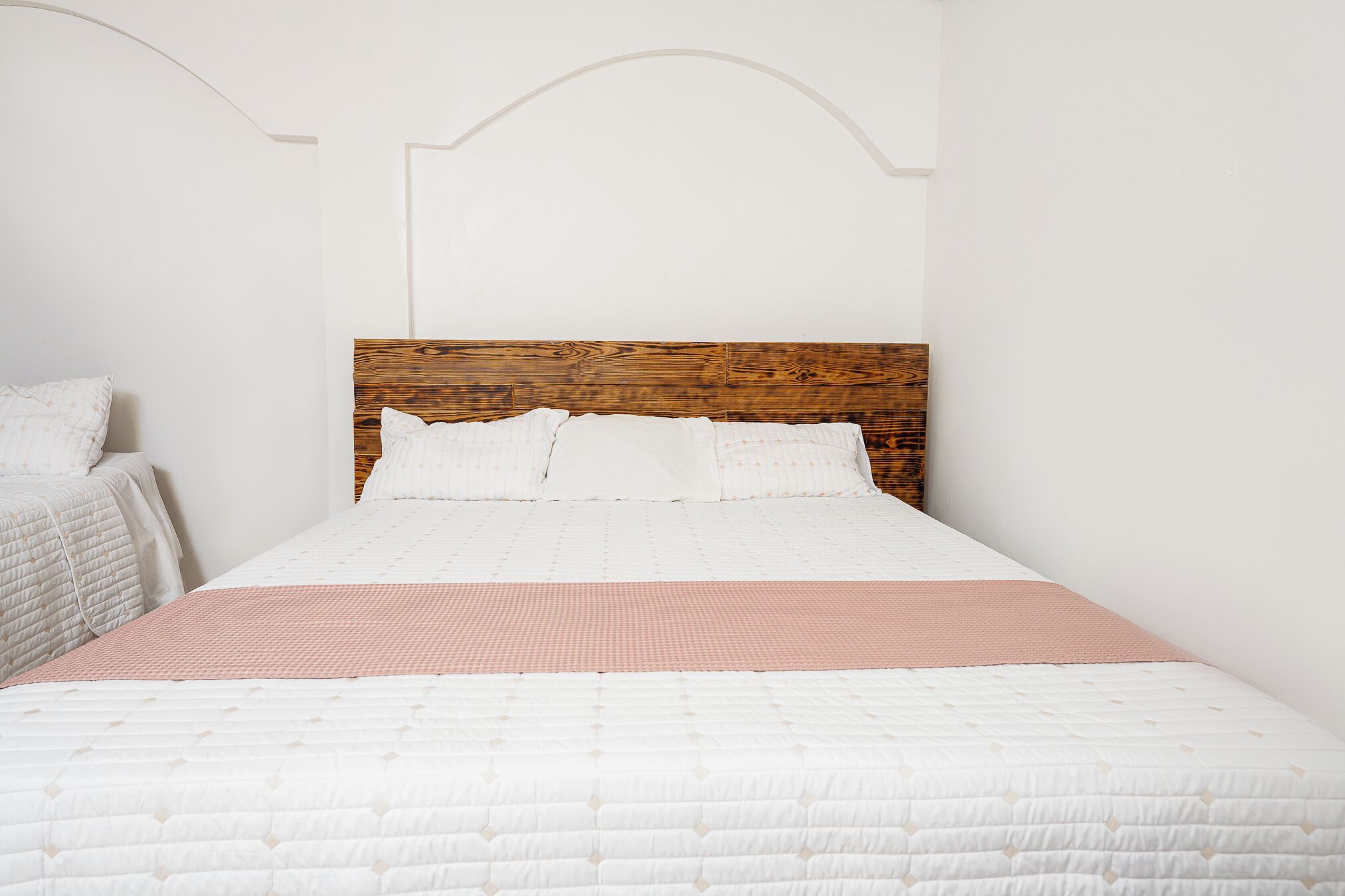 Una cama con cabecera de madera, ropa de cama blanca y una manta rosa.