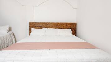 Una cama con cabecera de madera, ropa de cama blanca y una manta rosa.