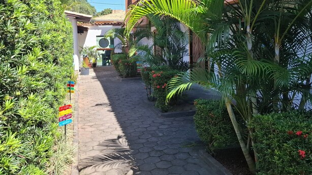 A pathway leading to a building with a tiled roof and surrounded by lush greenery and potted plants. - Mestre Lord aparthotel by La Vem Ferias  (Porto Seguro)