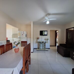 A living room with a TV, a ceiling fan, and a dining area with chairs and a table. - Mestre Lord aparthotel by La Vem Ferias  (Porto Seguro)