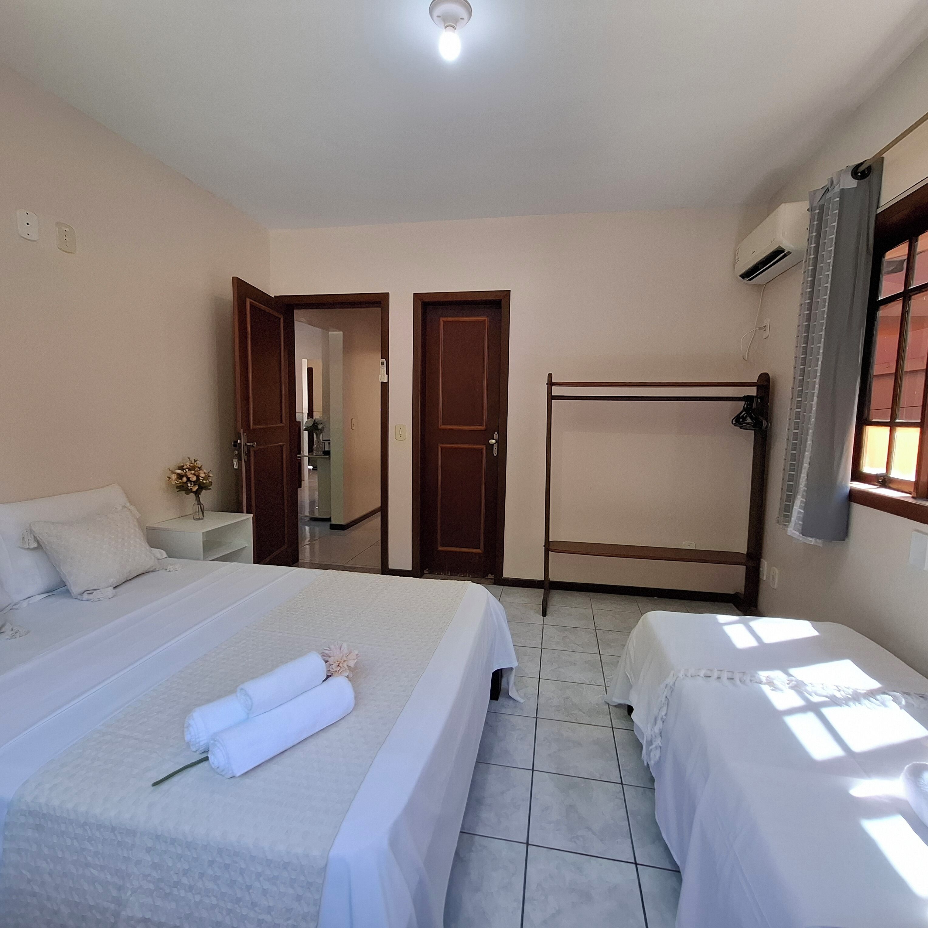 A hotel room with two beds, a wooden bench, a small table, and a window with curtains.
