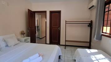 A hotel room with two beds, a wooden bench, a small table, and a window with curtains.