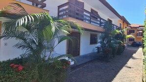 A two-story building with a balcony, a paved walkway, and surrounding greenery. - Mestre Lord aparthotel by La Vem Ferias  (Porto Seguro)