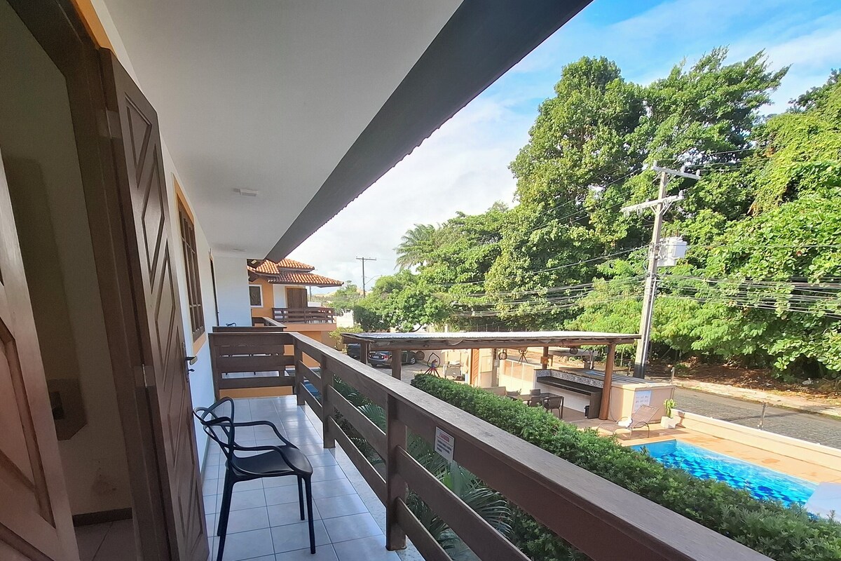 A balcony with a view of a swimming pool, a tiled floor, and a wooden railing.