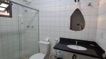 A bathroom with a glass shower enclosure, a white toilet, a black sink with a mirror above, and a trash bin.
