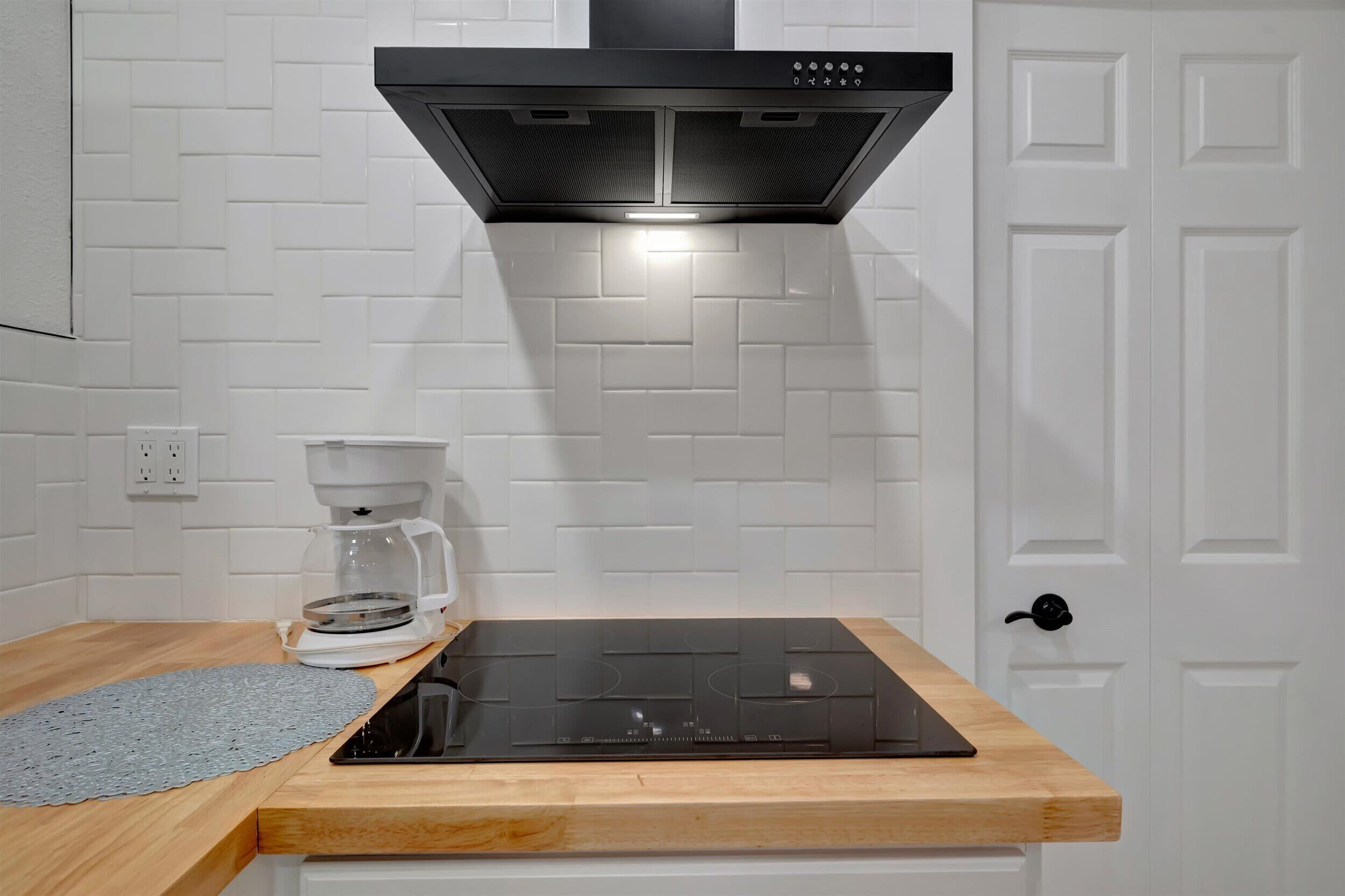 A kitchen with a black induction cooktop, a coffee maker, and a white tiled backsplash.