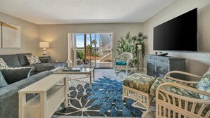 A living room with a sofa, armchair, coffee table, TV, and a staircase leading to an outdoor area. - Relax Beachside! Tropical Resort Amenities 1B1B (St. Petersburg)