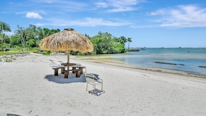 A beach with a thatched umbrella, wooden table, and lounge chairs. - Relax Beachside! Tropical Resort Amenities 1B1B (St. Petersburg)
