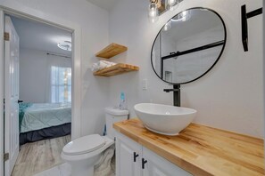 Een badkamer met een wit wastafel, houten planken, een ronde spiegel en een toilet.