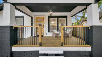 A covered porch with a wooden railing, a bench, and wicker furniture.