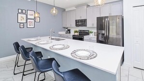 Una cucina moderna con isola centrale, sgabelli da bar, illuminazione a sospensione ed elettrodomestici in acciaio inossidabile.