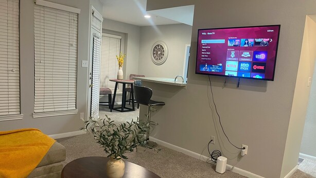 A living room with a flat-screen TV mounted on the wall, a dining area with a table and chairs, and a small plant on a round table. - Quiet Enjoyment in Houston Medical Center (Houston)