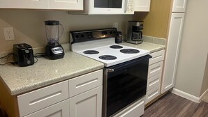 A kitchen with white cabinets, a white microwave, a black stove, a coffee maker, and a blender. - Quiet Enjoyment in Houston Medical Center (Houston)