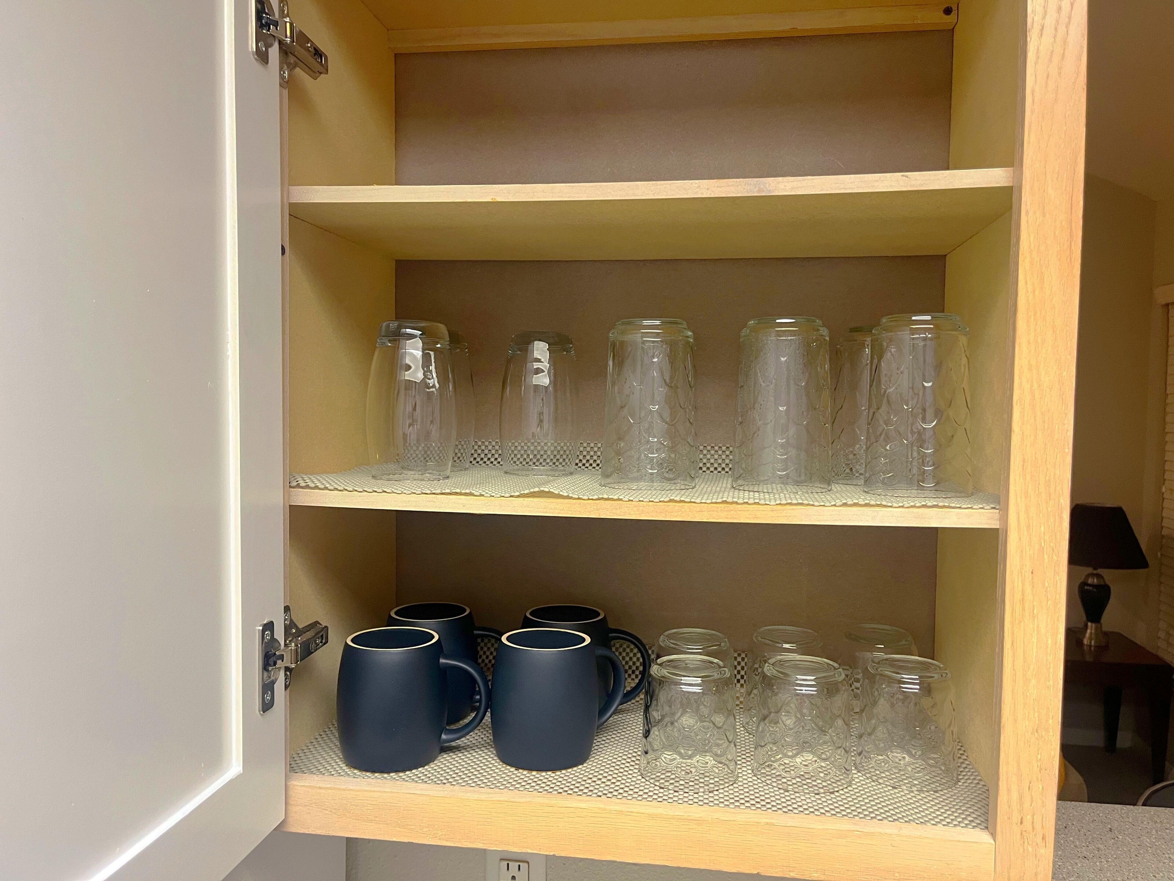 Un meuble en bois doté d’étagères où sont rangés des bocaux en verre transparent et des tasses noires.