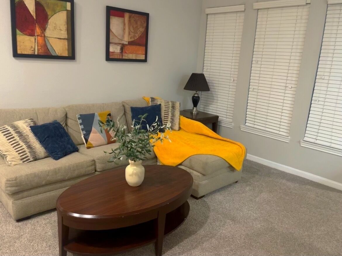 A living room with a sofa, a coffee table, a lamp, and a window with blinds.