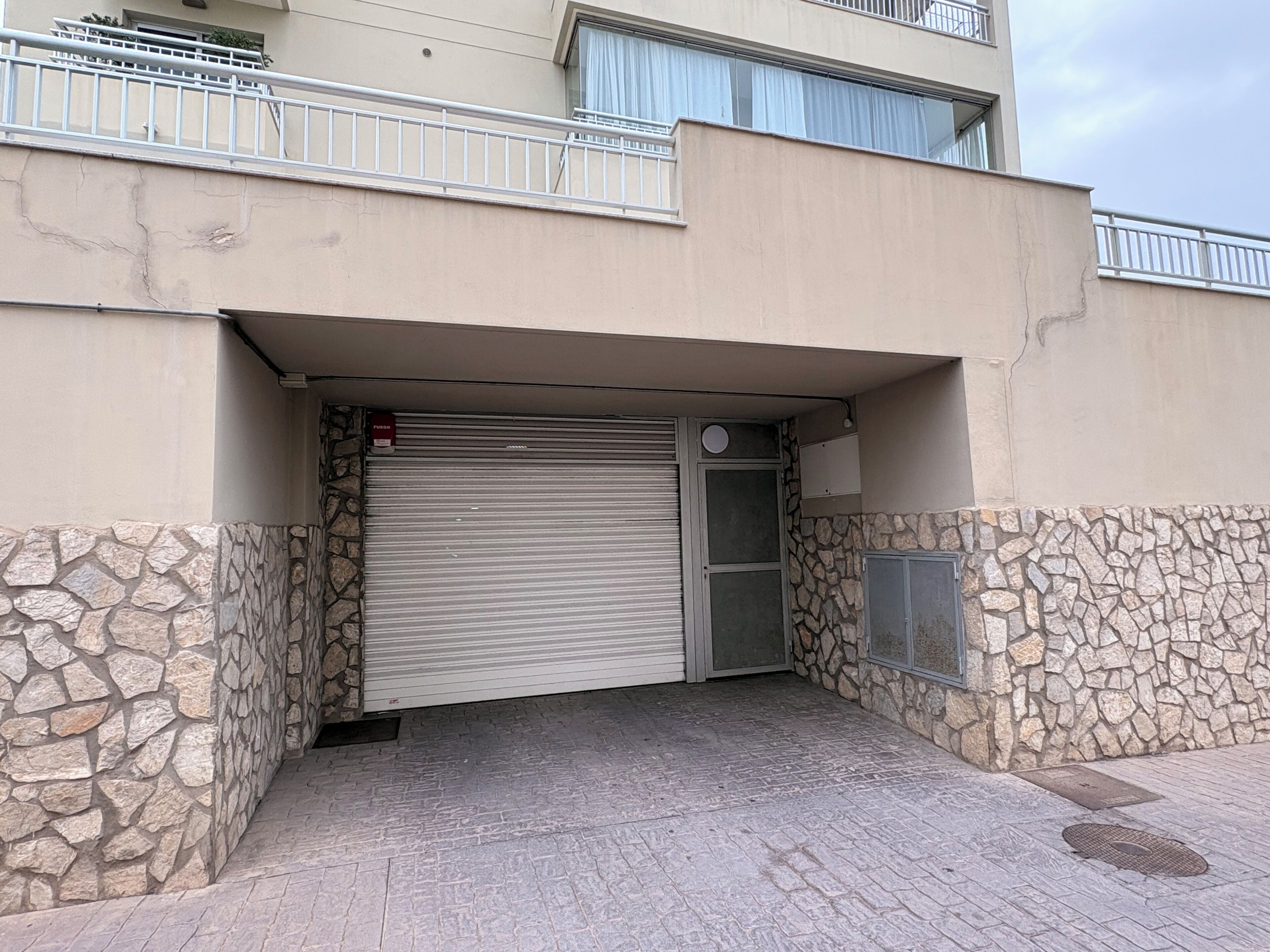 A building entrance with a closed metal shutter, stone walls, and a metal railing on the upper level.