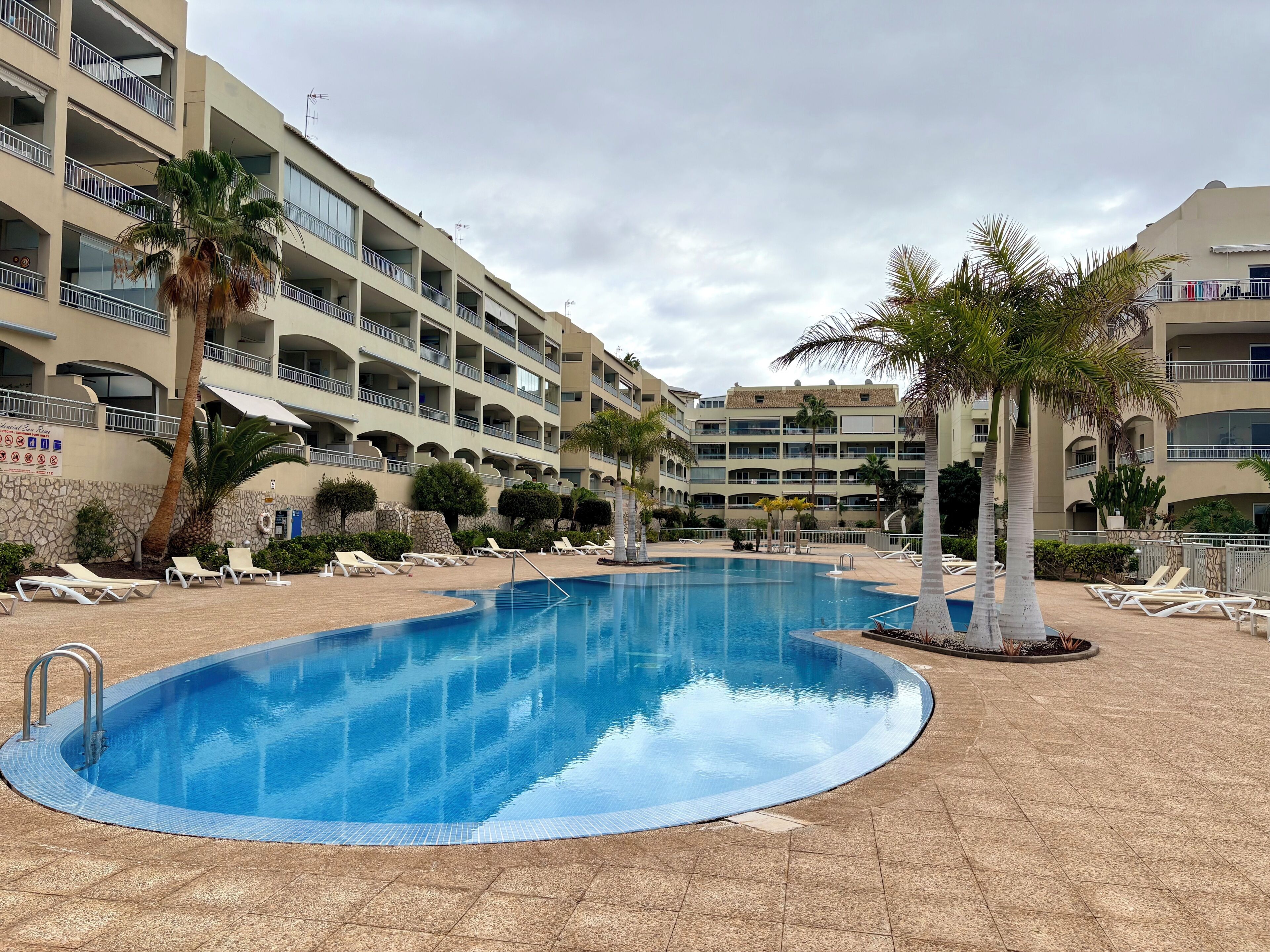 A hotel with a swimming pool, multiple balconies, and palm trees.