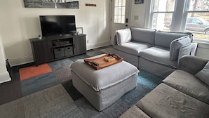 A living room with a sectional sofa, a television, and a window with a view of the outside. - Perfect 1-bedroom house in vibrant Minneapolis (Minneapolis)