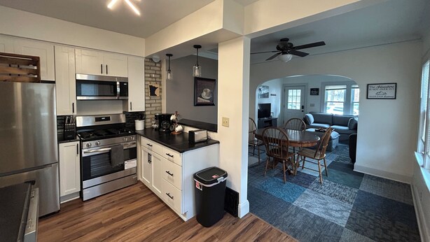 A modern kitchen with stainless steel appliances, a dining area with a wooden table and chairs, and a living room with a sofa and a ceiling fan. - Perfect 1-bedroom house in vibrant Minneapolis (Minneapolis)