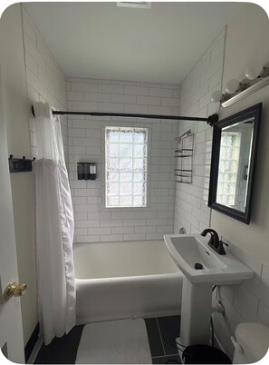 Ein Badezimmer mit Badewanne, Waschbecken, Toilette, einem Fenster mit Milchglas und einer Duschvorhang.
