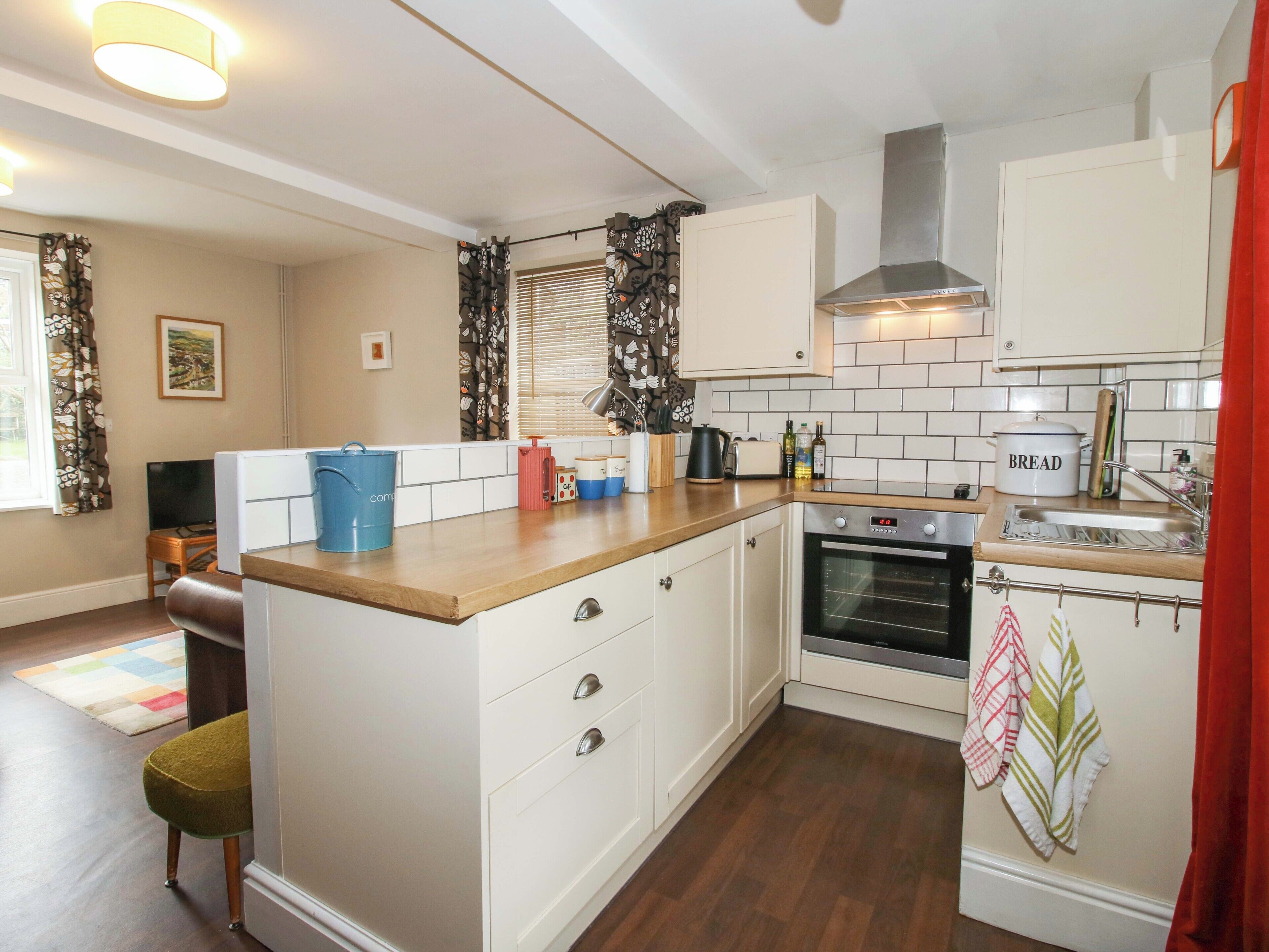 A kitchen with white cabinets, a wooden countertop, a built-in oven, and a window with curtains.