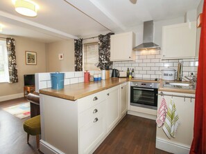 A kitchen with white cabinets, a wooden countertop, a built-in oven, and a window with curtains. - Little Pentwyn (Hereford)
